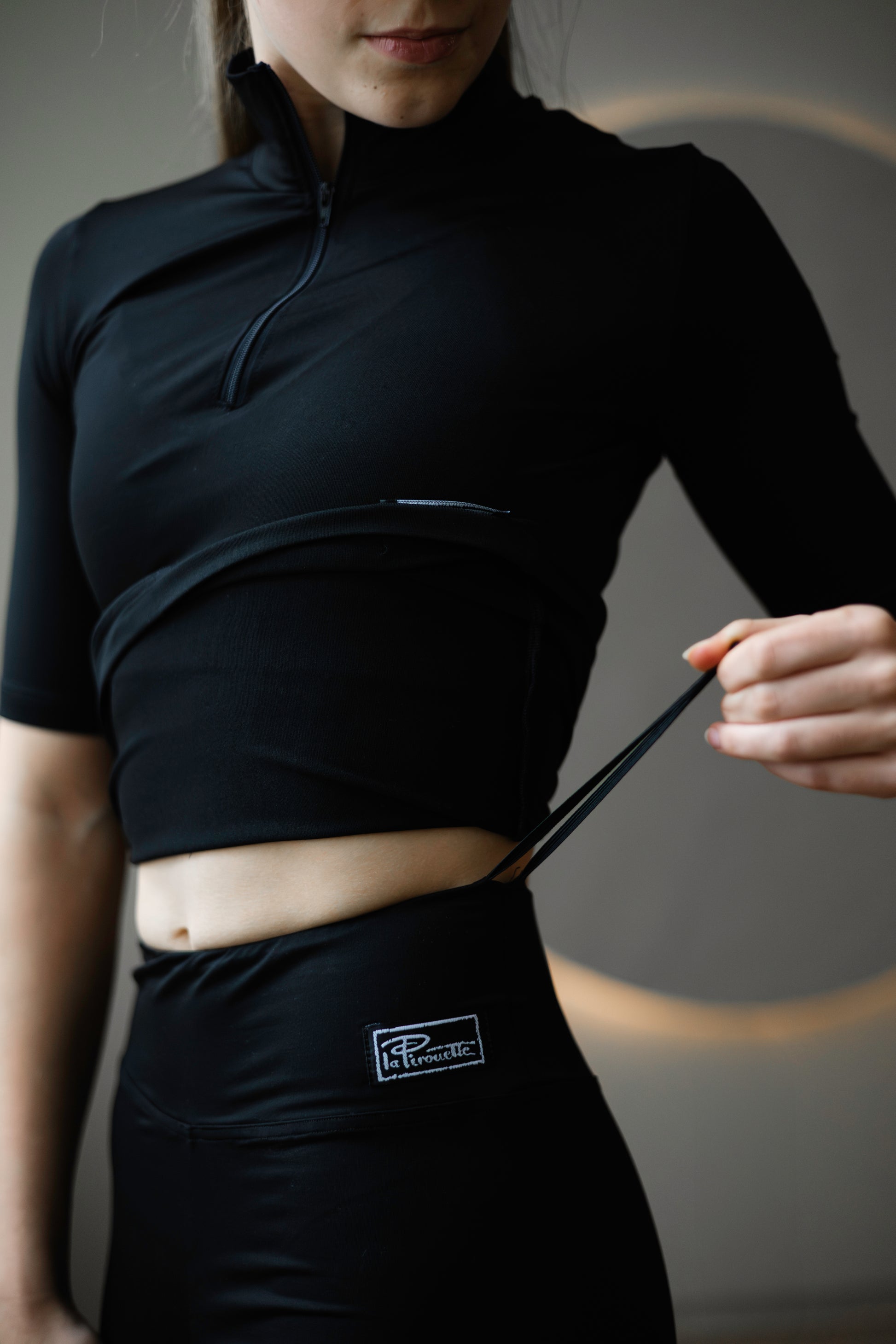 Person wearing a black outfit with a visible brand logo, holding a black string.